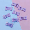 Several bone-shaped hair clips in light purple are arranged on a light blue and pink background.