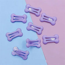 Plusieurs pinces à cheveux en forme d'os de couleur violet clair sont disposées sur un fond bleu clair et rose.