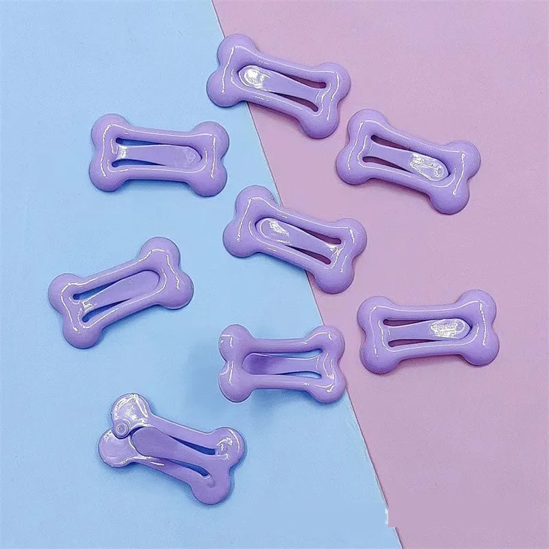Several bone-shaped hair clips in light purple are arranged on a light blue and pink background.