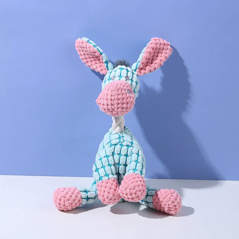 A pink and blue squeaky plush donkey dog toy with large ears and a textured body is displayed against a light purple backgrou