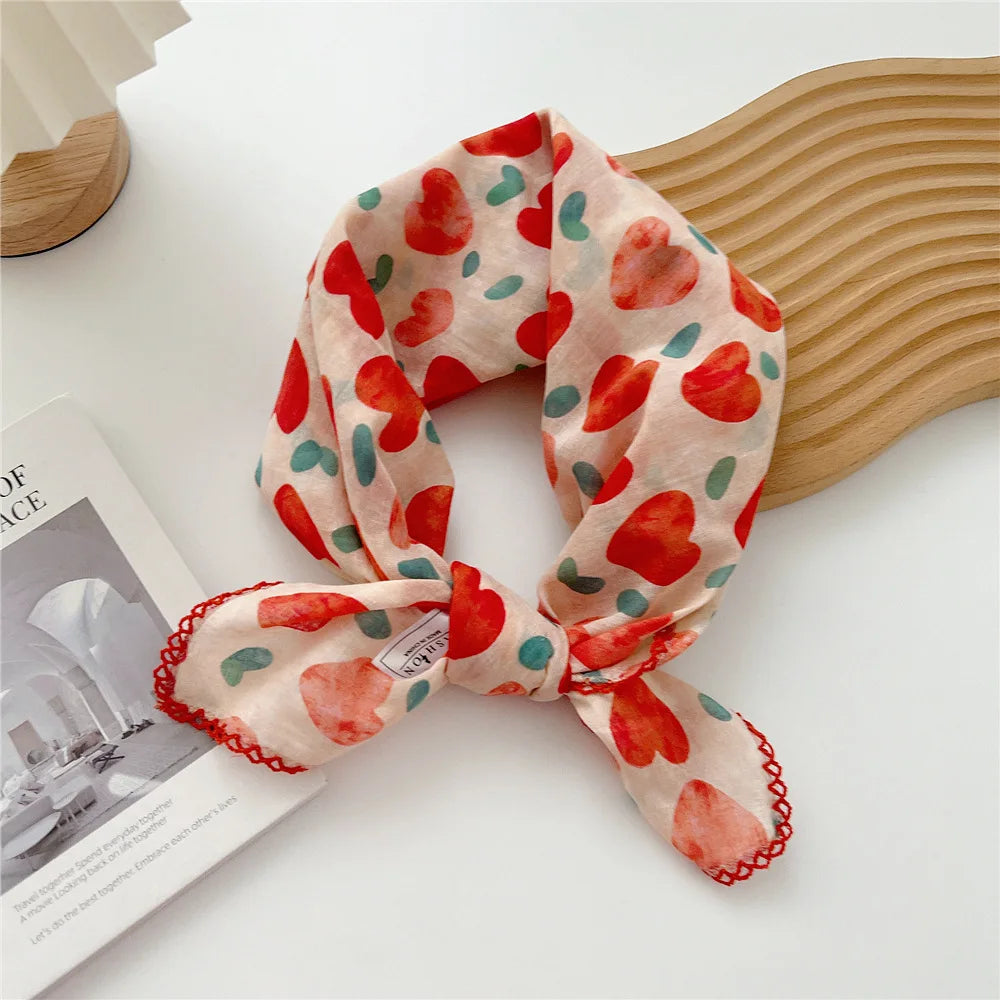 Écharpe en coton rose avec motif floral de cœurs rouges et verts, présentée sur une surface claire.
