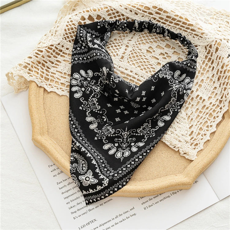 Black and white bohemian paisley triangle head scarf draped on a light beige fabric background