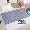 A blue diamond patterned waterproof bed protector pad is laid on a white bed with a white pillow and a beige blanket.