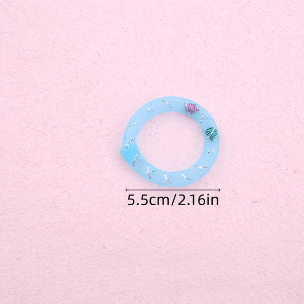A light blue, circular mesh chew toy with small pink and green accents is shown on a pink background.