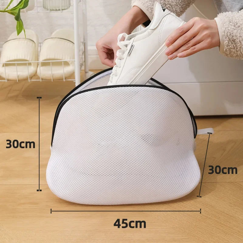 Una bolsa de ropa de malla blanca reutilizable junto a un par de zapatillas blancas en un suelo de madera.