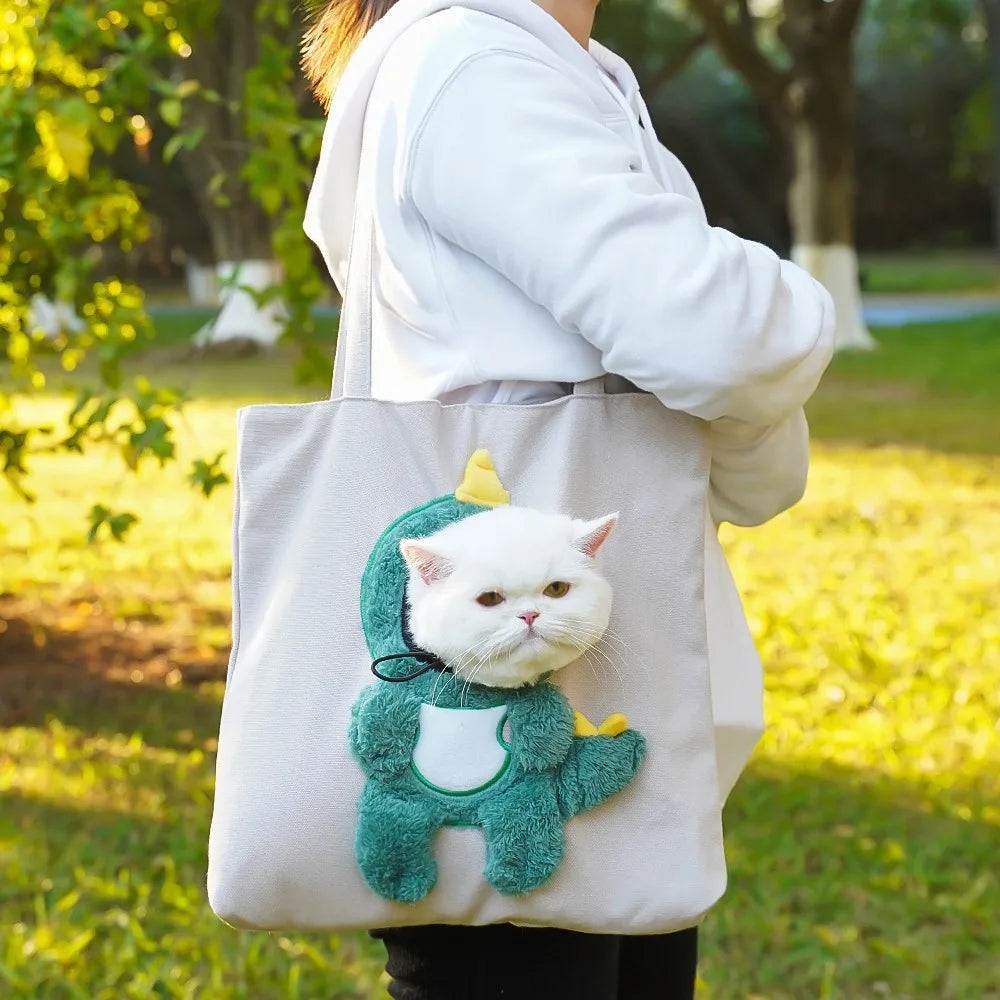 A person is holding a light beige portable crossbody pet carrier bag featuring a green stuffed cat.