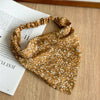 Diadema o pañuelo de pelo con estampado floral boho amarillo mostaza, apoyado en un libro de color claro.