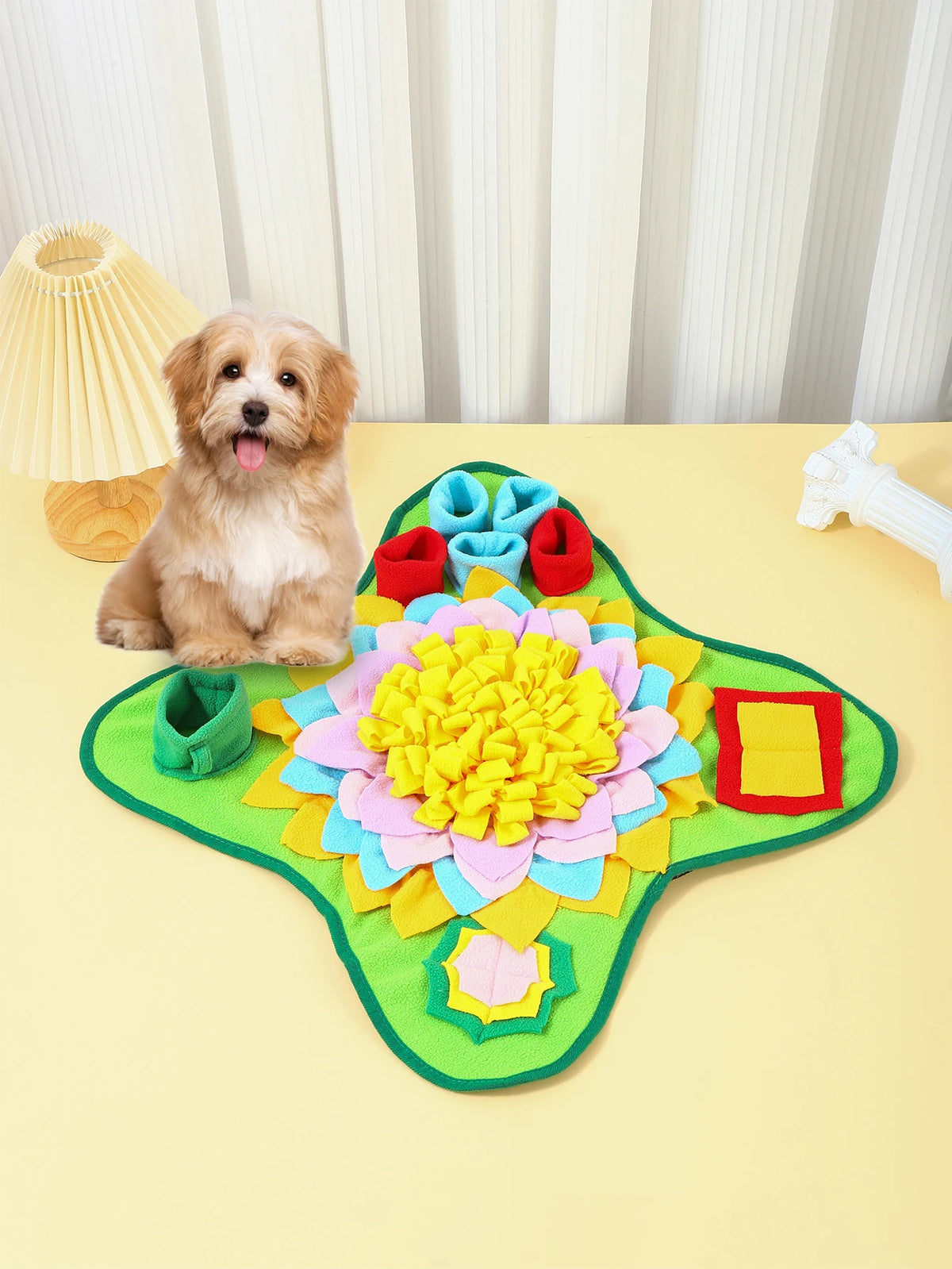 A golden-colored dog is sitting next to a green snuffle mat decorated with colorful fabric flowers.