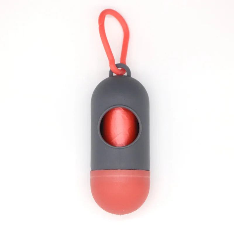 A capsule-shaped dog poop bag dispenser with a gray body and red base, attached to an orange carabiner clip.