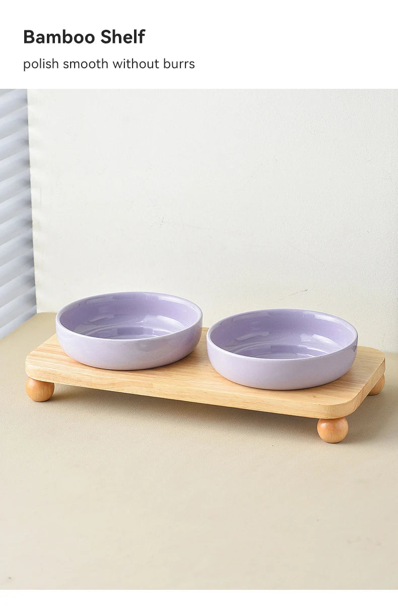 A light purple ceramic bowl is placed on a natural wood shelf, used as a stand for a pet bowl.