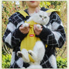 A person is holding a yellow cycling walking pet carrier for cats with a white cat in an outdoor setting.