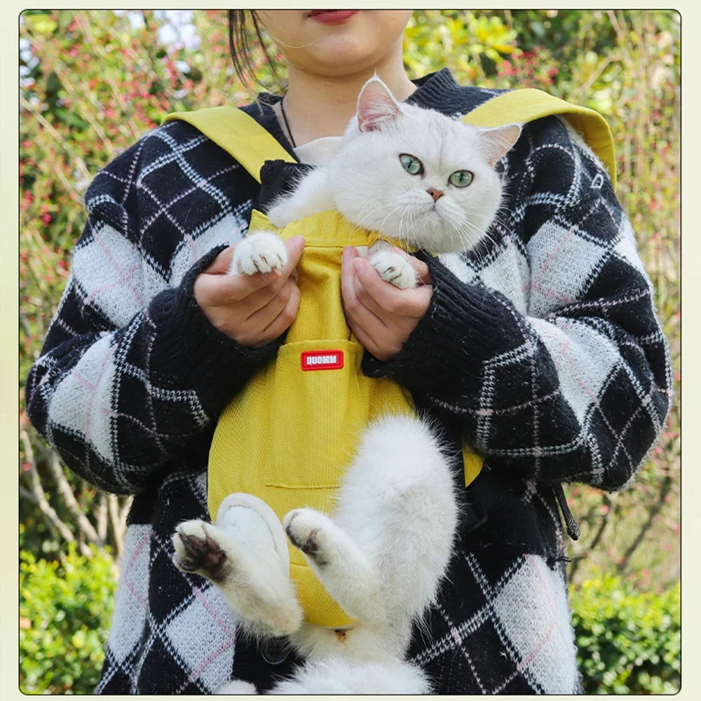A person is holding a yellow cycling walking pet carrier for cats with a white cat in an outdoor setting.