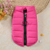 A bright pink quilted padded dog coat jacket with a black zipper and silver hardware lying on a light fabric surface.
