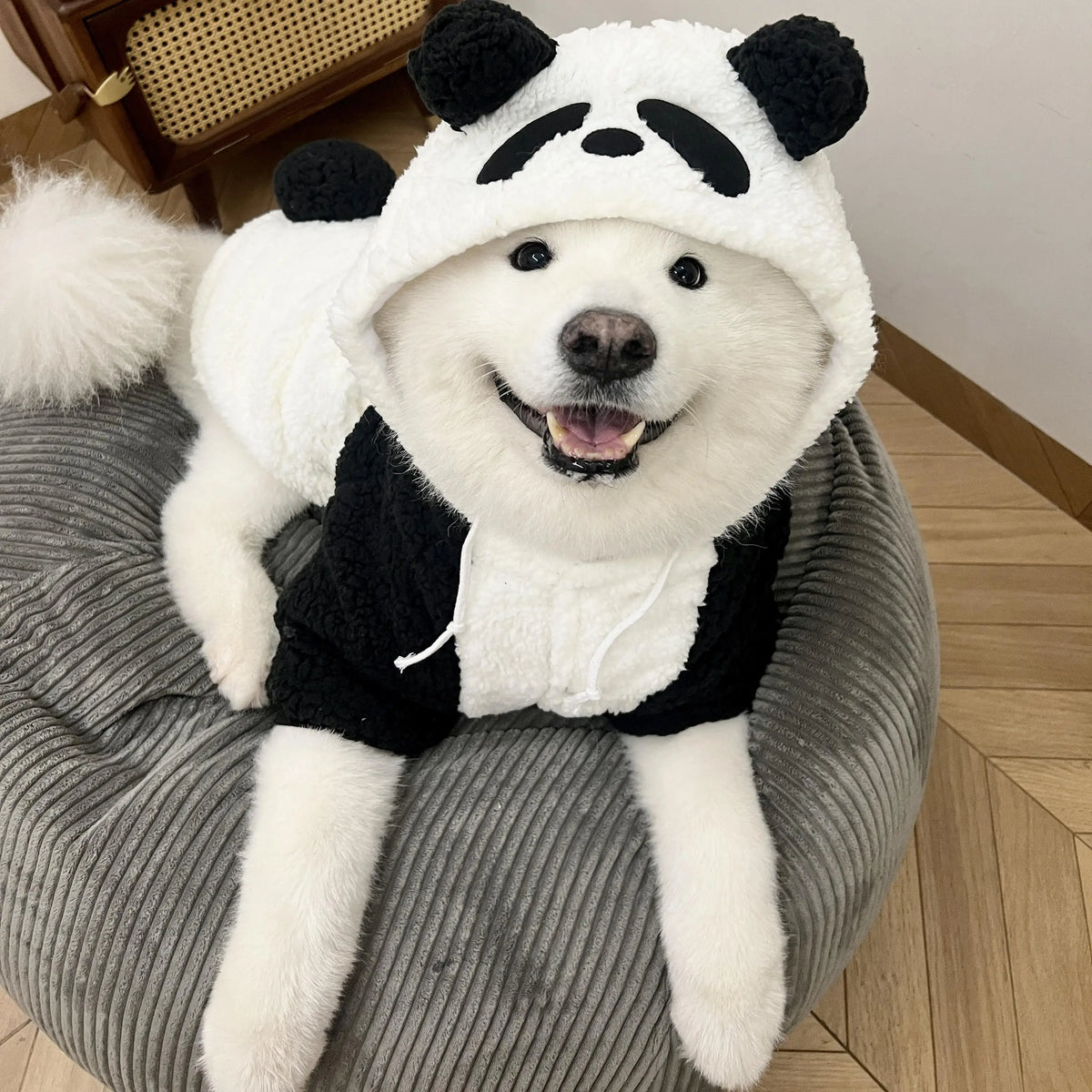 A white panda-themed fleece dog coat with black accents sitting on a gray fabric.