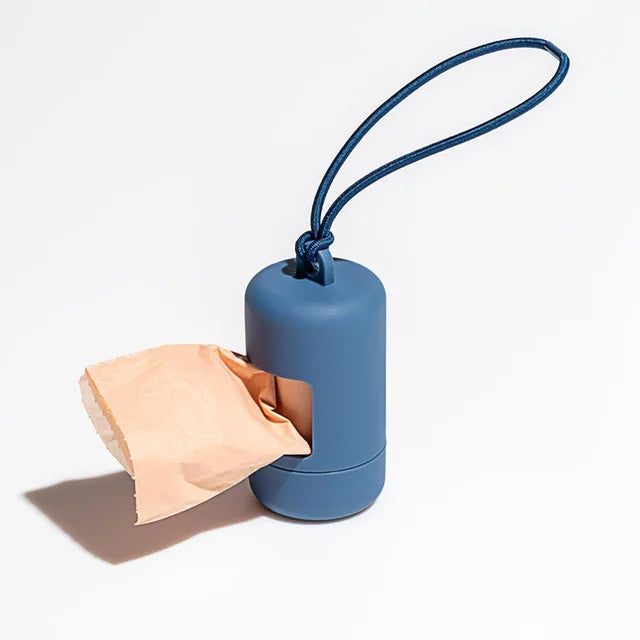 A blue portable dog poop bag dispenser with a thin blue strap and a piece of tan paper visible.