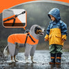 A child wearing an orange and gray reflective waterproof dog raincoat stands next to a dog in the rain.
