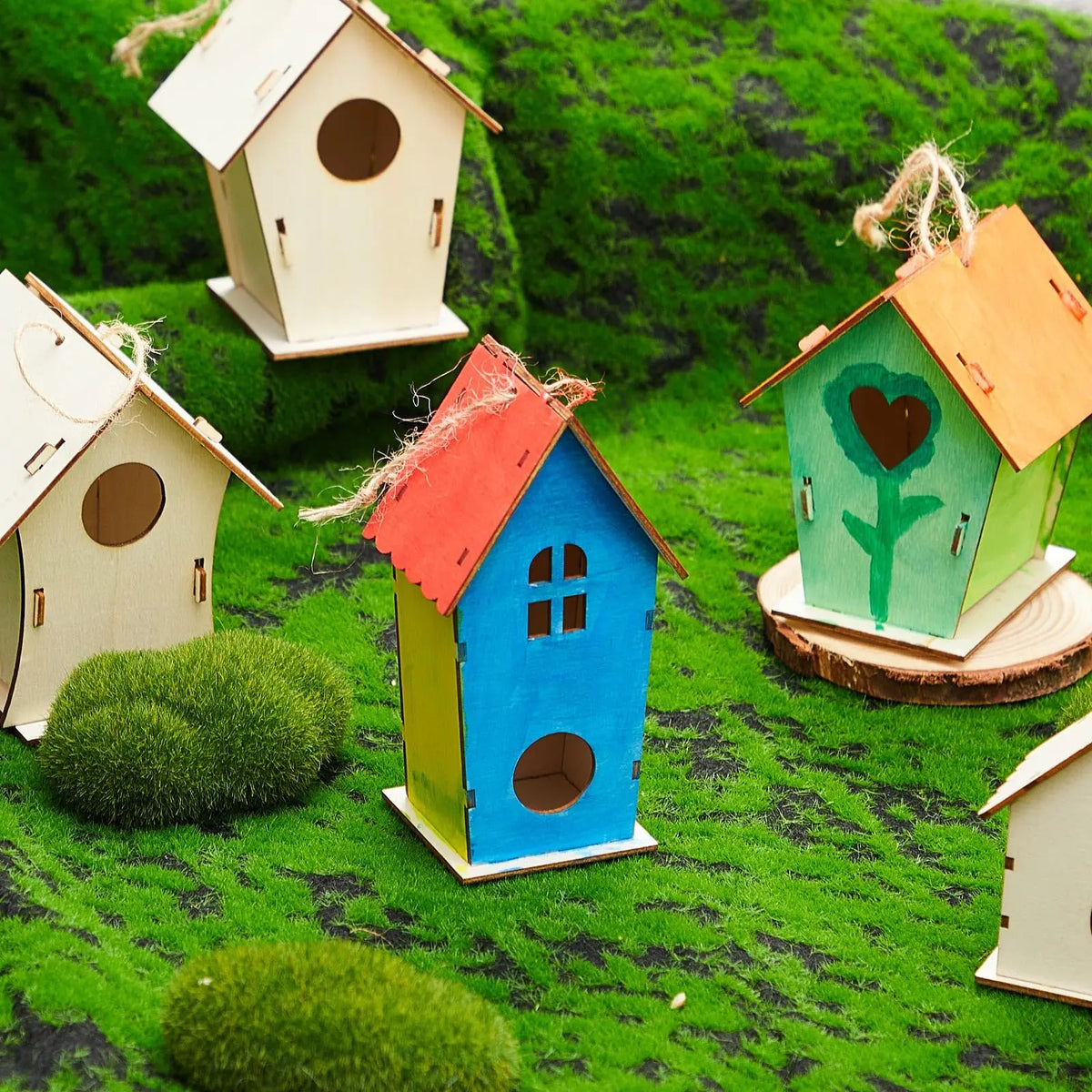 Colorful wooden bird houses of various sizes and colors placed in a green grassy landscape.