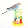 Ein kleiner blau-grauer Lovebird sitzt auf einem gelben Puzzlespielzeug mit bunten Ringen.