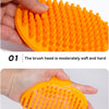 A hand is holding an orange rubber pet grooming brush, showing the soft and hard teeth of the brush head.