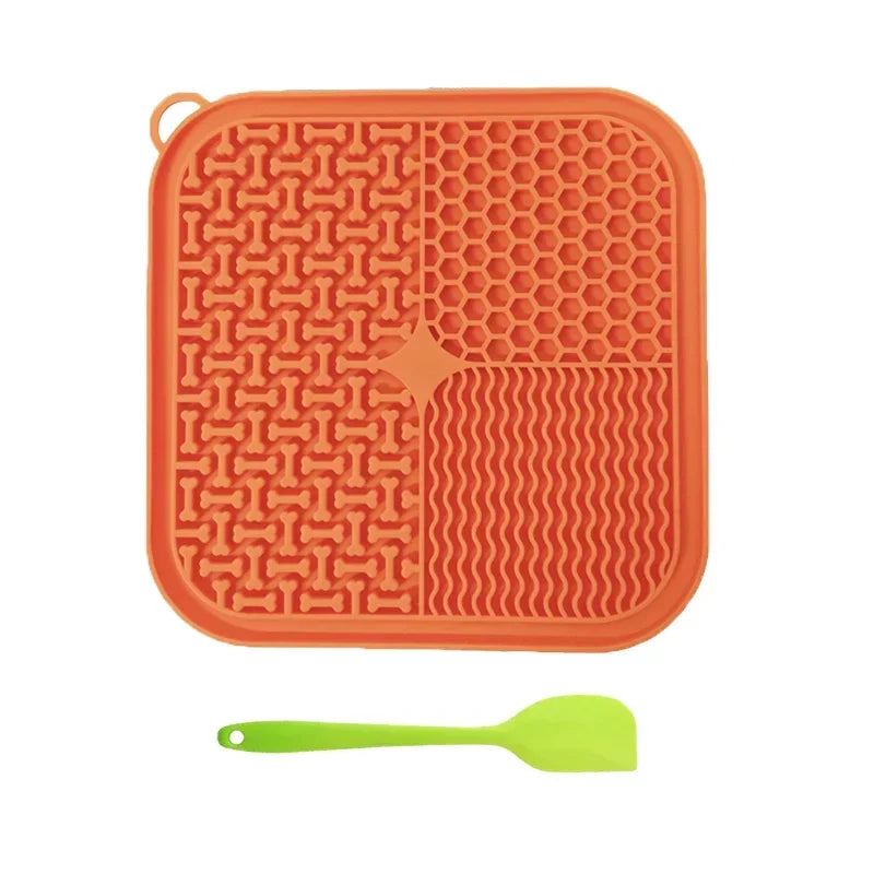 An orange silicone licking mat for pets featuring various textured patterns and a green silicone spoon.