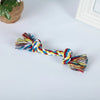 A colorful braided cotton rope dog chew toy with tassels lying on a white surface.