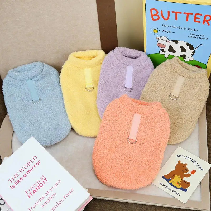 Colección de suéteres de invierno para perros de felpa cálida en varios colores pastel, dispuestos en una caja.