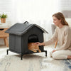 A woman is interacting with a dark gray heated outdoor cat shelter designed for pets.