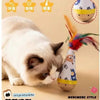 A white cat is looking at an interactive feather wobble ball toy with a small wooden figure.