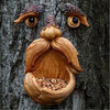 A handcrafted resin bird feeder shaped like a tree, featuring carved eyes and a nest filled with seeds.