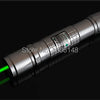 A silver laser pointer with a green beam shining across a dark surface.