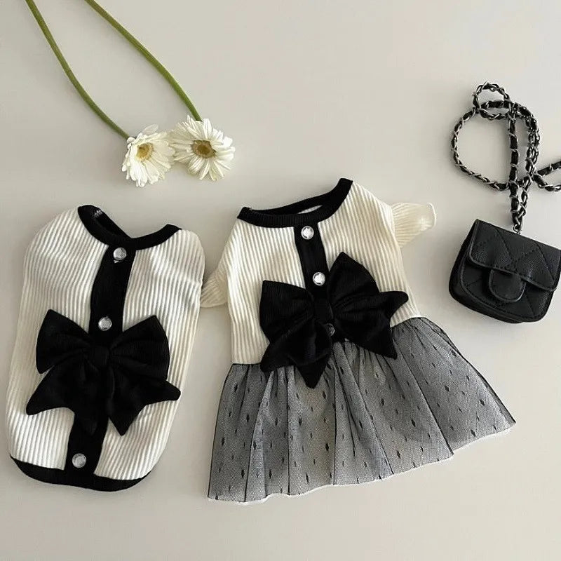 A white and black striped dress for a small dog featuring a large black lace bow on the bodice and a sheer gray tulle skirt.