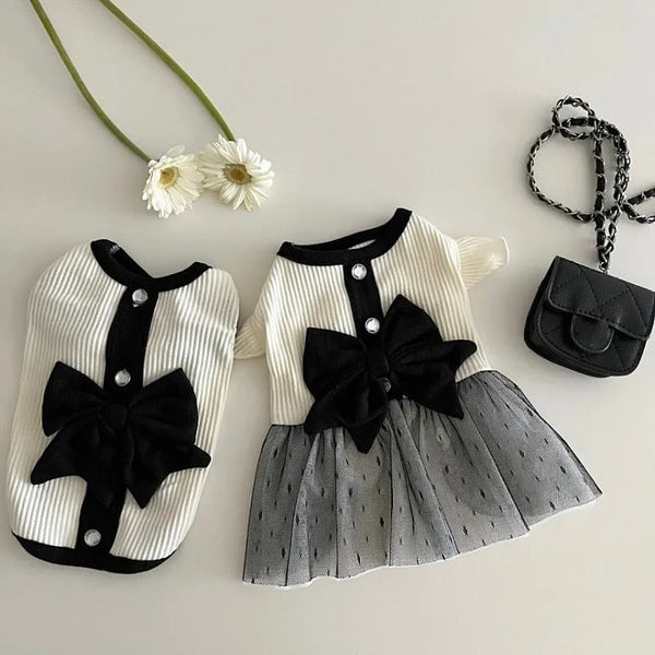 A white and black striped dress for a small dog featuring a large black lace bow on the bodice and a sheer gray tulle skirt.