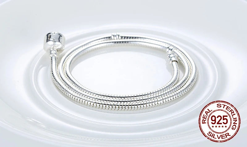 A silver snake chain necklace with a heart charm displayed on a white plate.