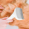 A hand is using a white pet slicker brush on the fur of an orange dog.