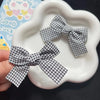 A pair of black and white plaid fabric bows used as hair clips, displayed on a white plate.