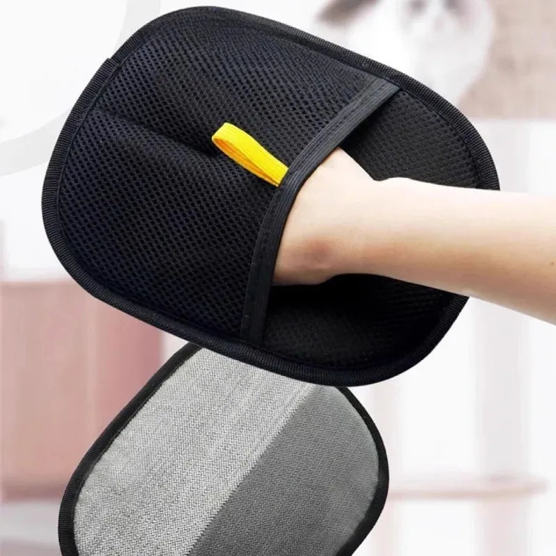 A hand is wearing a black double-sided pet grooming glove with a yellow finger tip, resting on a gray pad.