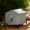 A gray pet bed with a sloping roof and an arched entrance is placed outdoors on a wooden surface.