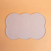 A white silicone pet feeding mat with an irregular, scalloped edge placed on a light orange background.