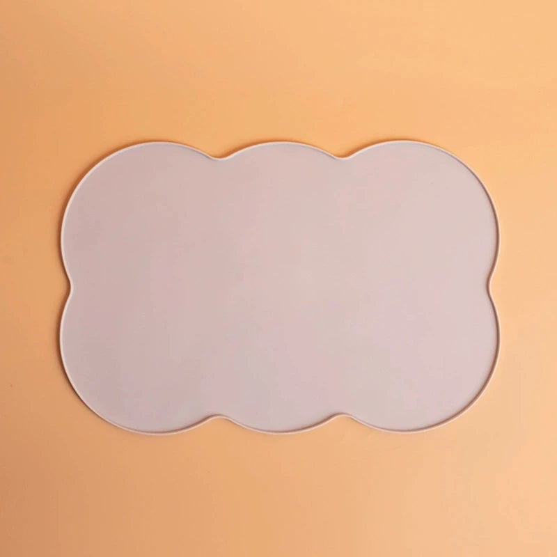 A white silicone pet feeding mat with an irregular, scalloped edge placed on a light orange background.