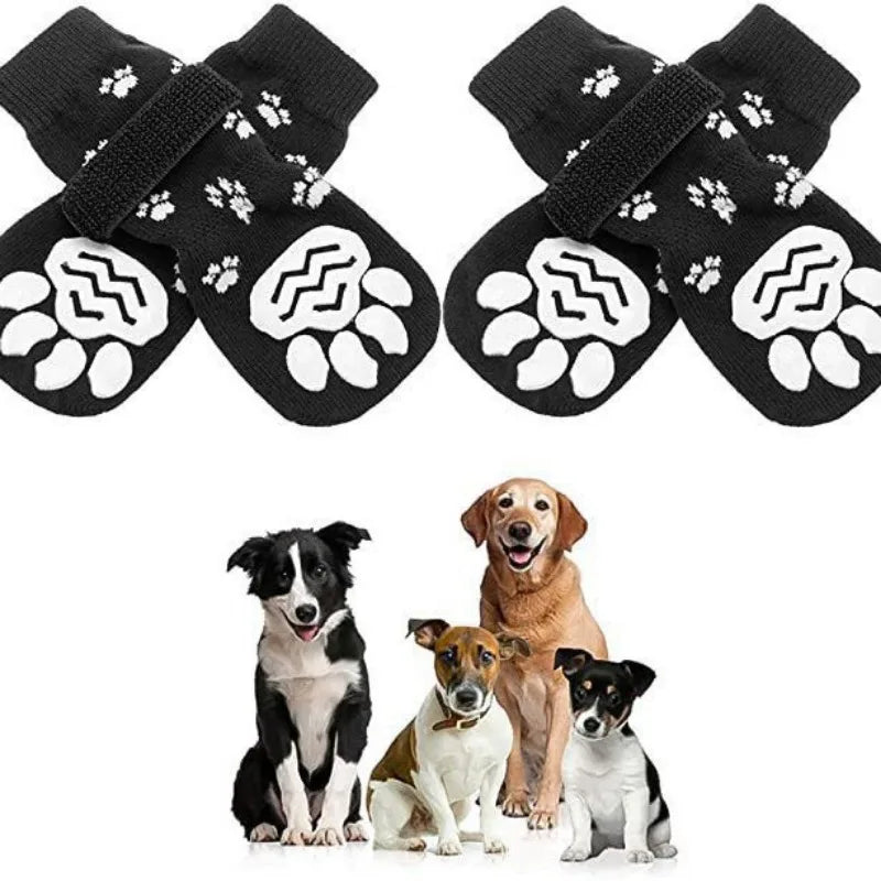 A pair of black anti-slip dog socks with traction straps lying next to a group of dogs.