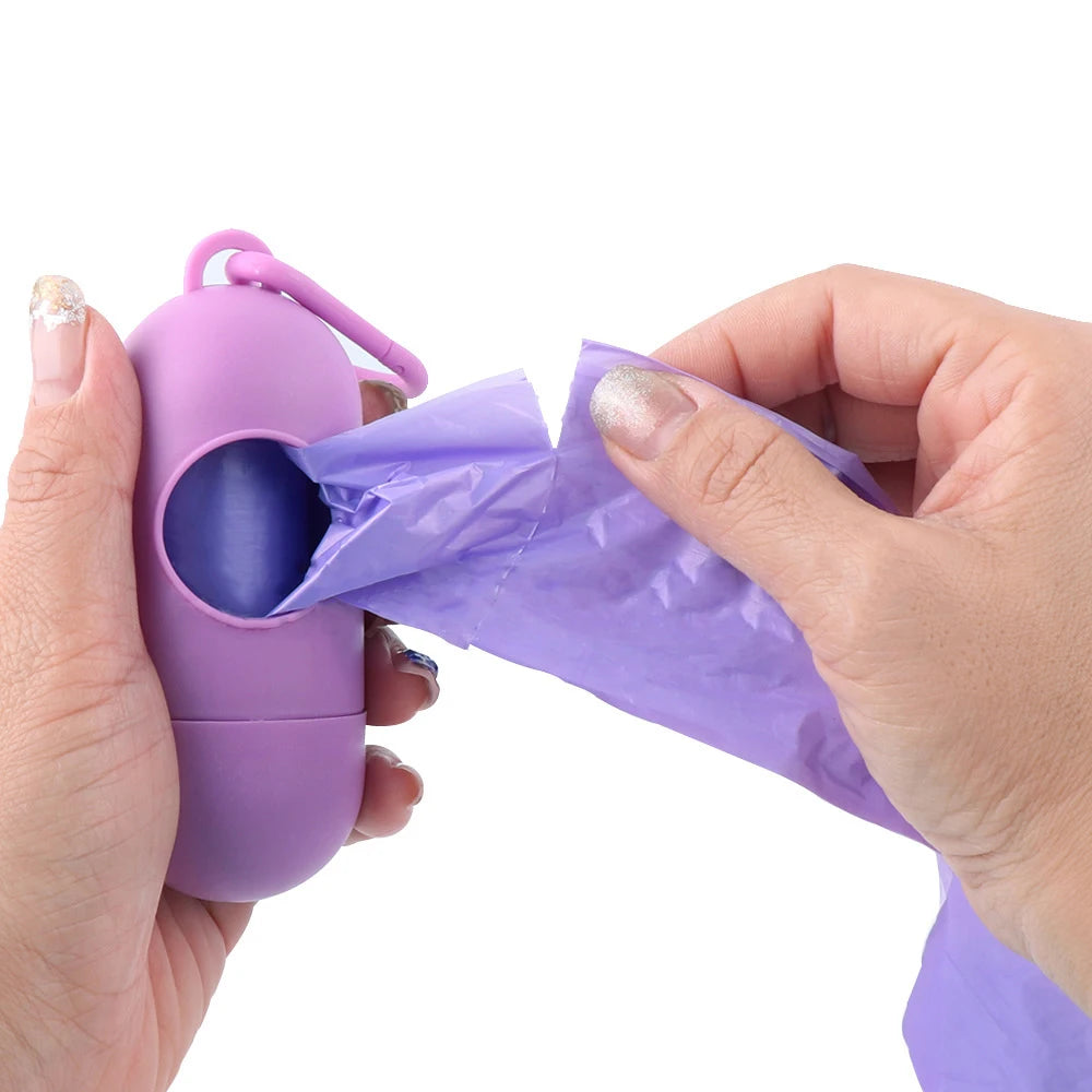 A hand is holding a purple capsule-shaped dog poop bag dispenser with a carabiner clip and a crumpled purple plastic bag.
