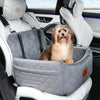 A fluffy golden dog is sitting in a gray plush car seat inside a white car, viewed from the back seat.