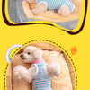 A fluffy light-colored dog wearing a striped cotton recovery suit with anti-lick protection, resting in a soft, beige fabric 