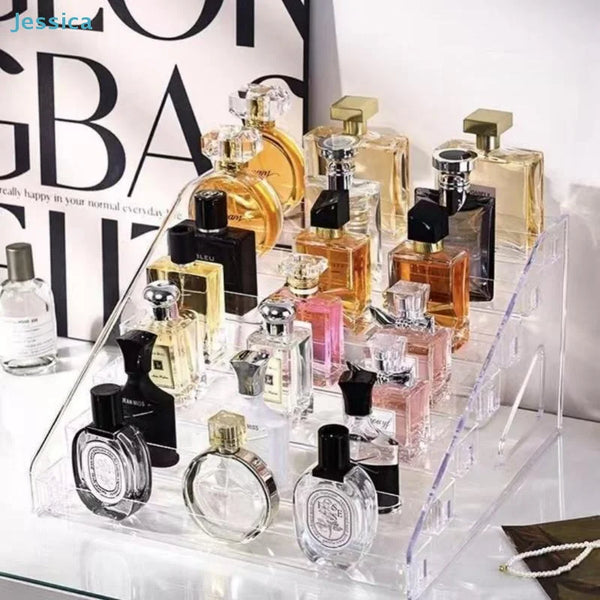 Clear acrylic display stand holding various perfume bottles and glass containers.