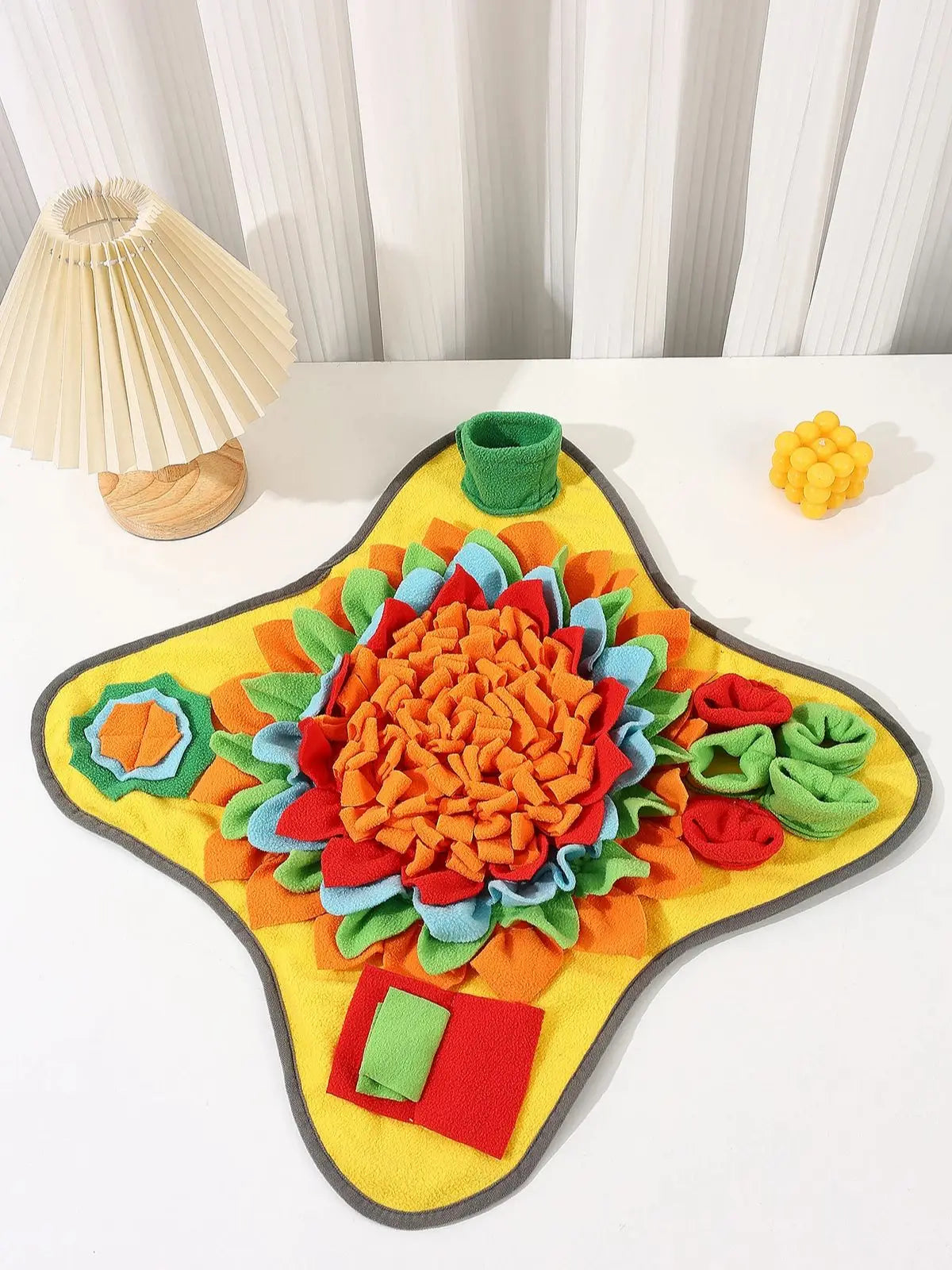 A colorful, textured snuffle mat for dogs featuring various fabric pieces in orange, green, red, and yellow.