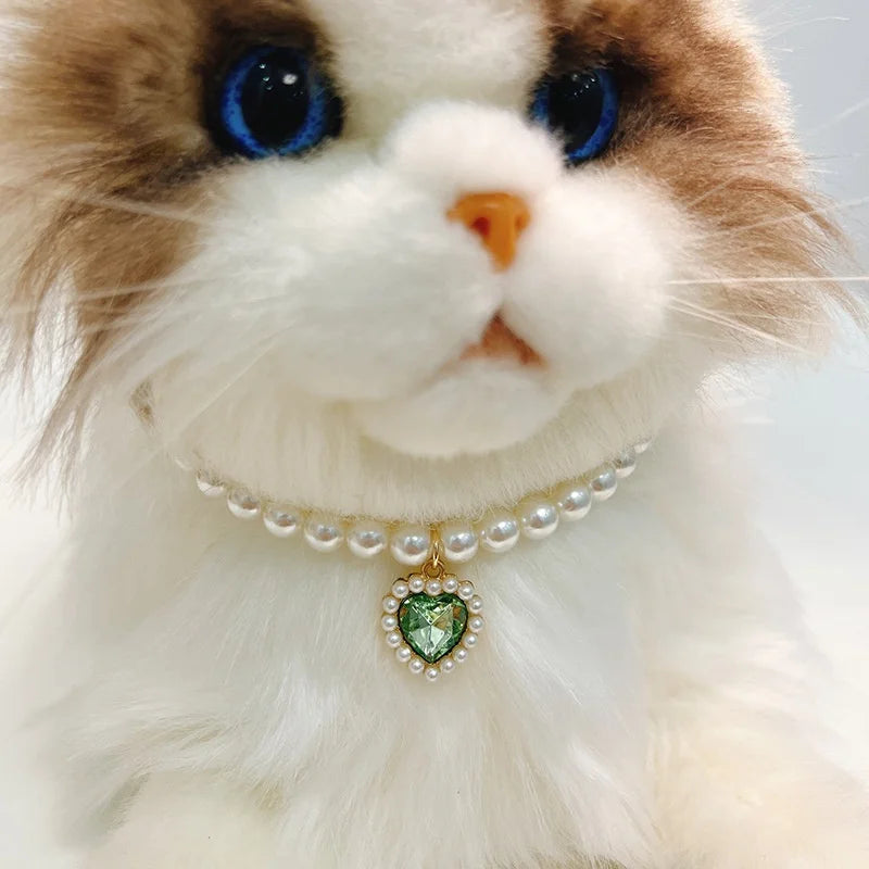 A fluffy brown and white cat wearing a pearl collar with a green gemstone pendant.