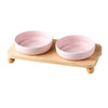 A pink ceramic cat and dog bowl set with a wooden stand.
