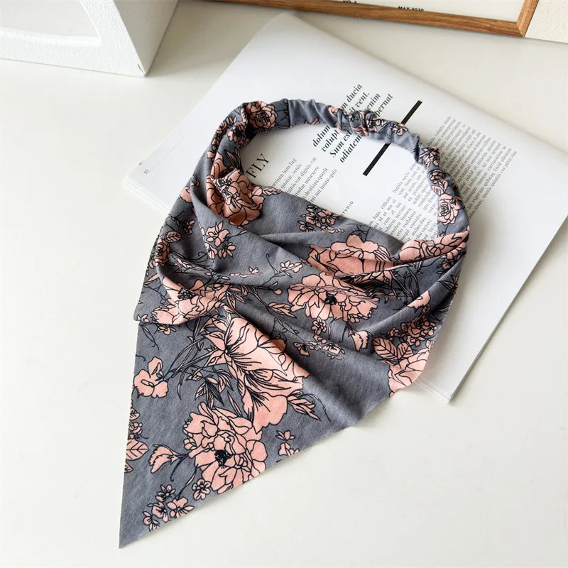 Una bufanda de tela gris con estampado floral en tonos rosa polvoriento y verde, drapeada sobre papel blanco.