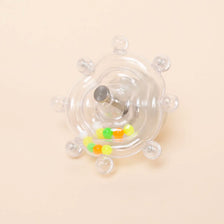 An interactive rotating parrot toy and treat dispenser with a clear plastic body and small colored treats.