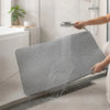 A hand is pouring water onto an extra-large double-layer cat litter mat with a honeycomb texture in a bathroom setting.